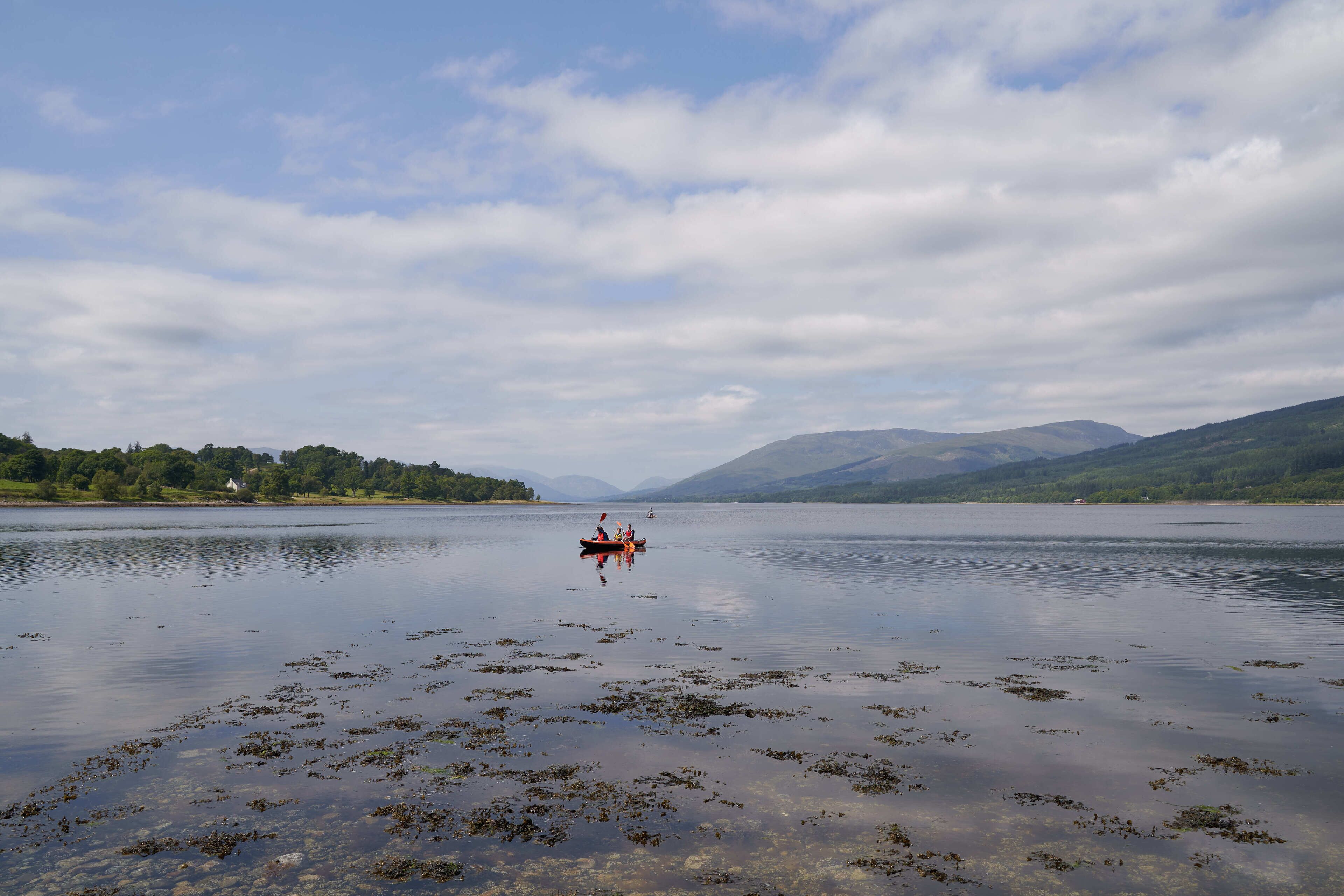 A calm lake with a small boat in the distance, surrounded by mountains and greenery.