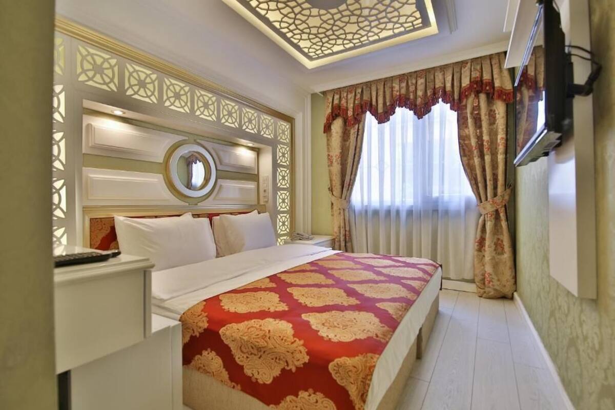 A hotel room with a large bed, a TV mounted on the wall, and a decorative ceiling.