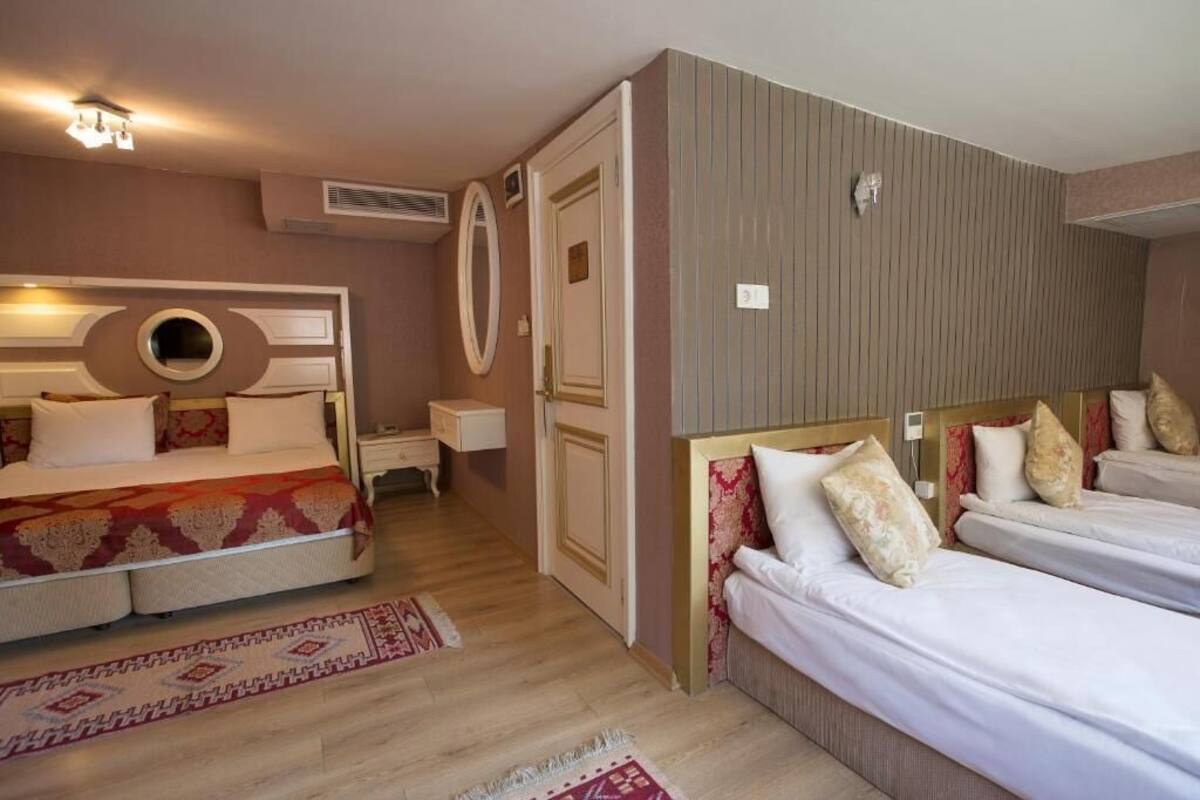 A hotel room with a large bed, two smaller beds, a mirror, a nightstand, and a wall-mounted air conditioning unit.