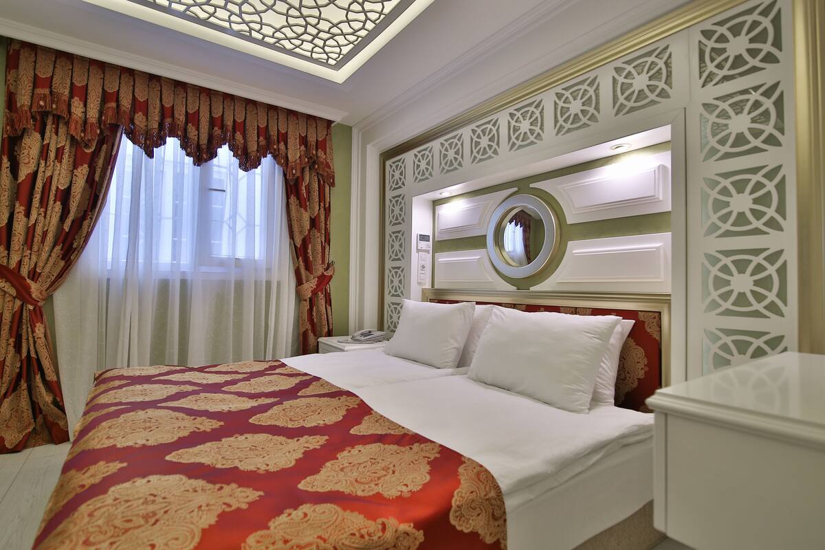 A hotel room with a large bed, a nightstand, a mirror, and decorative wall panels.