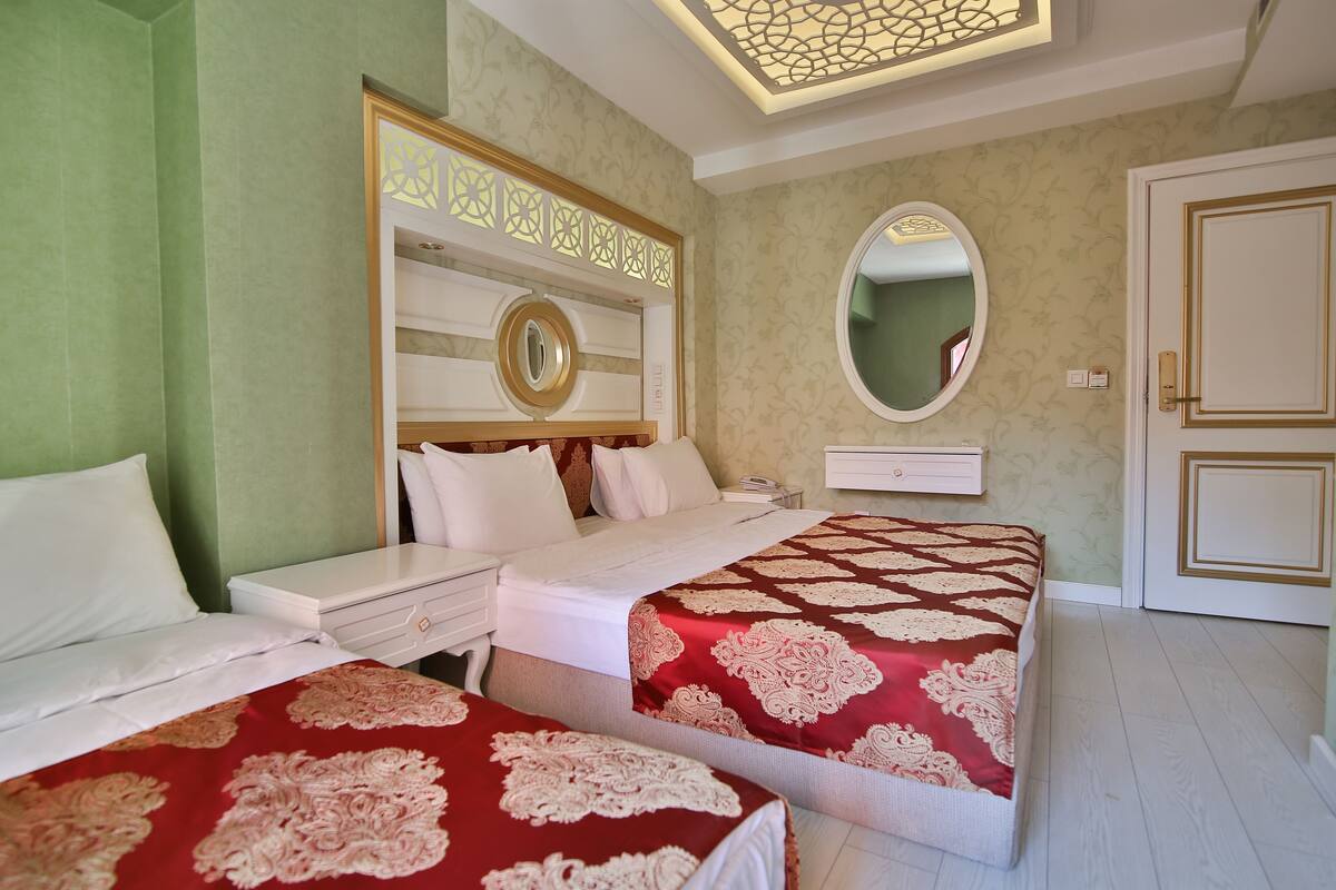 A hotel room with two beds, a nightstand, a mirror, and a wardrobe.