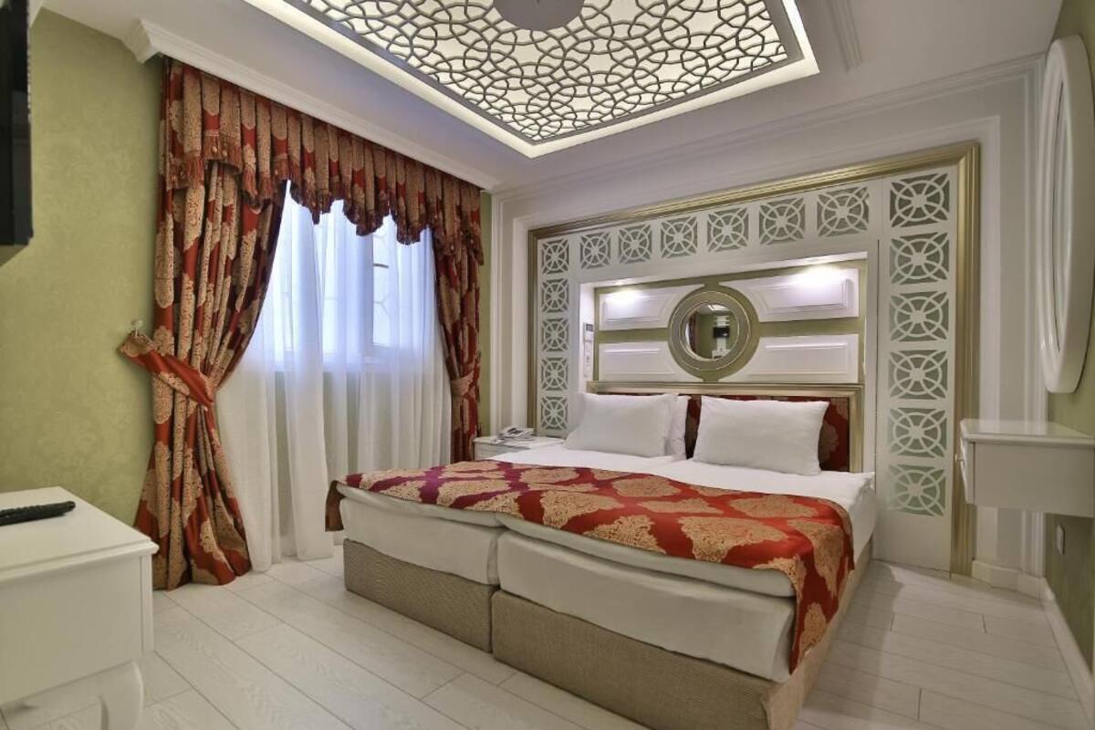 A hotel room with a large bed, a bedside table, a mirror, and a decorative ceiling.