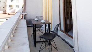 Un balcon avec une table et des chaises, une fenêtre avec des rideaux et une balustrade.