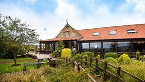 A building with a red-tiled roof, a wooden deck, and a garden with various plants and a bench. - The Stables Whitby (Whitby)