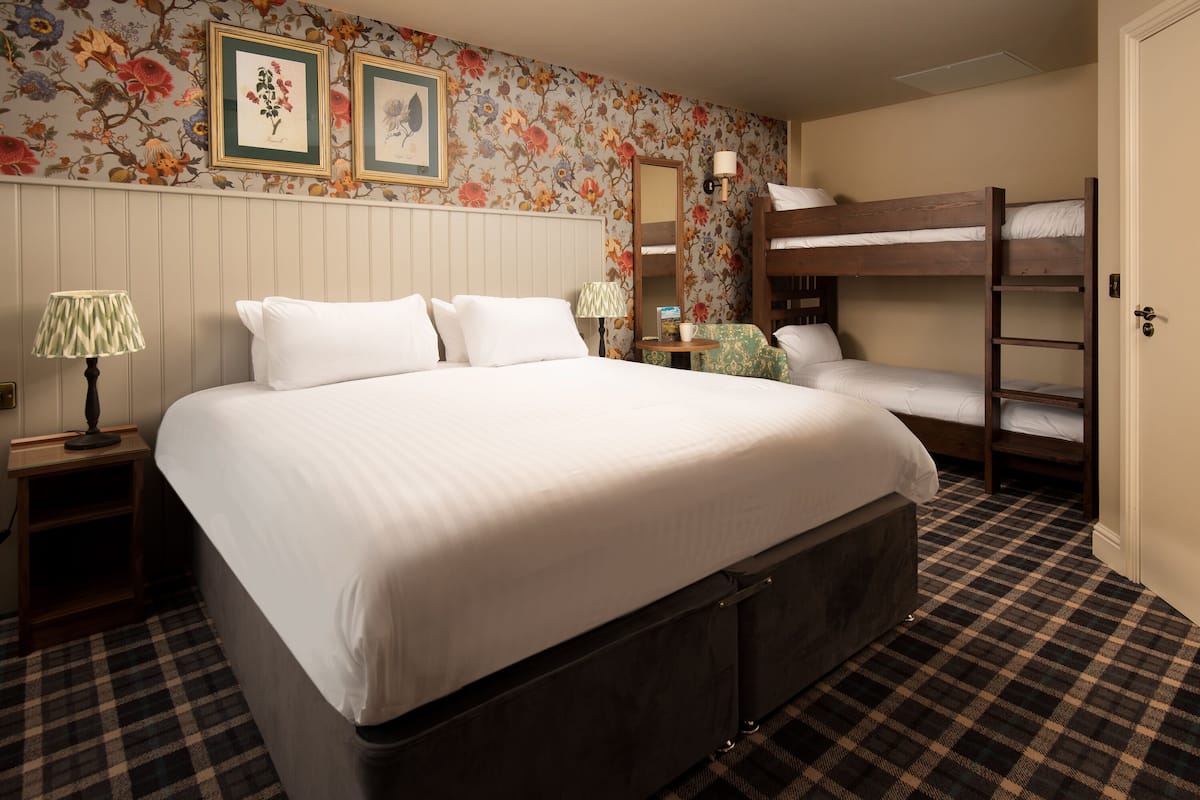 A hotel room with a large bed, a bunk bed, a mirror, a lamp, and a floral wallpaper.