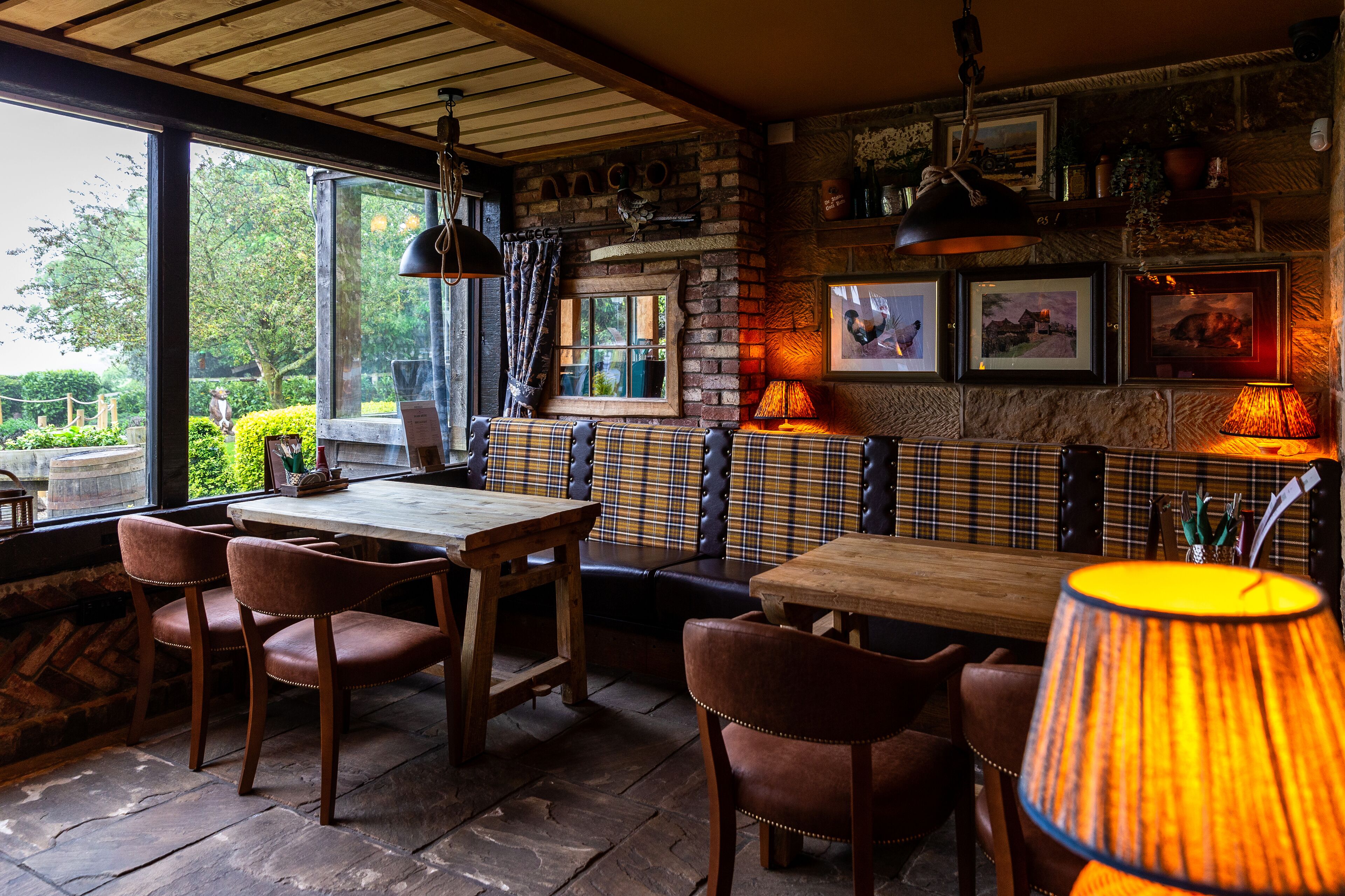 Un restaurant chaleureux, doté de meubles en bois, d’un espace détente avec des banquettes et offrant une vue sur la verdure environnante.
