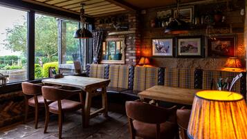 Un restaurant chaleureux, doté de meubles en bois, d’un espace détente avec des banquettes et offrant une vue sur la verdure environnante.