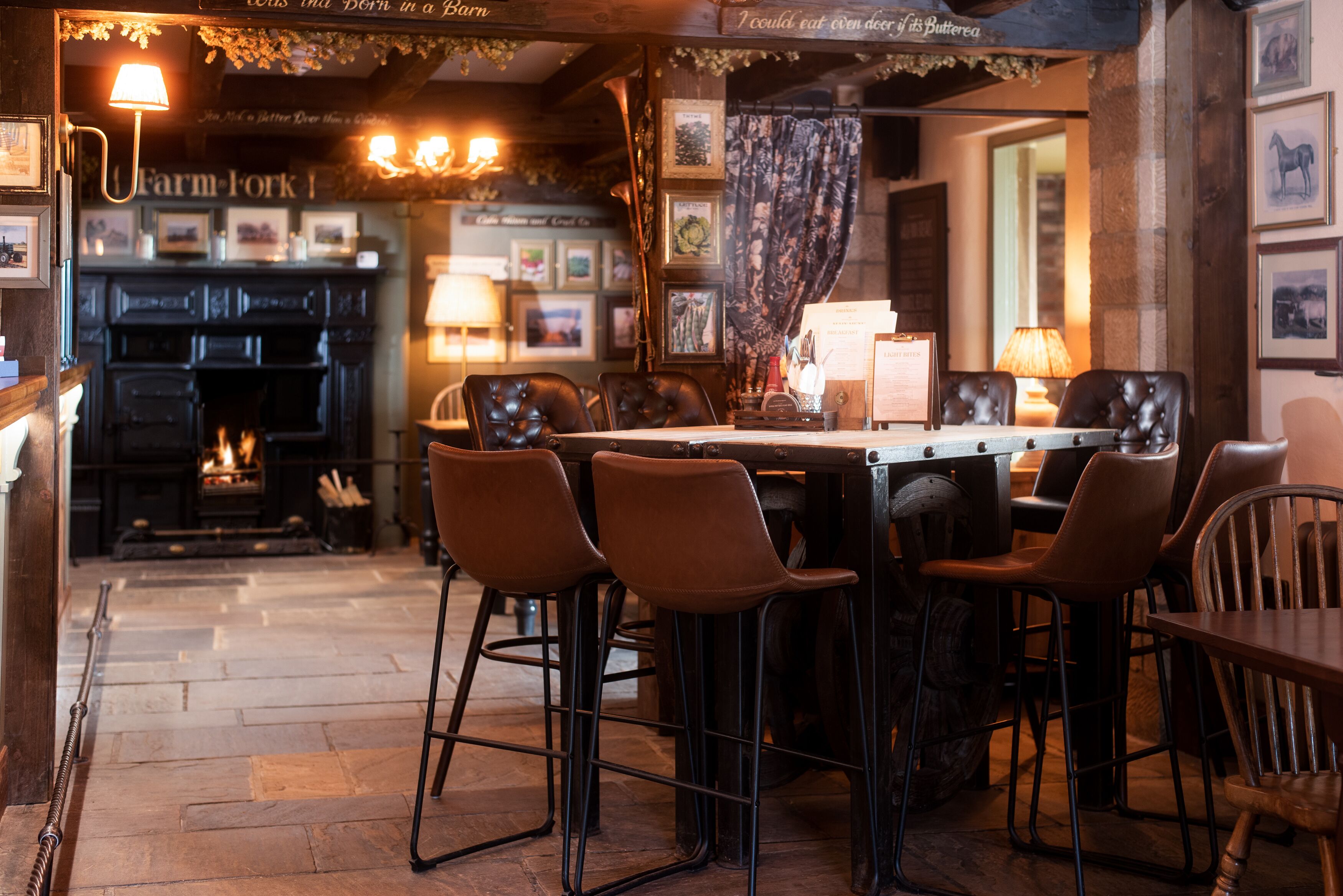 Un rincón acogedor con bar, chimenea, taburetes y una mesa de madera.