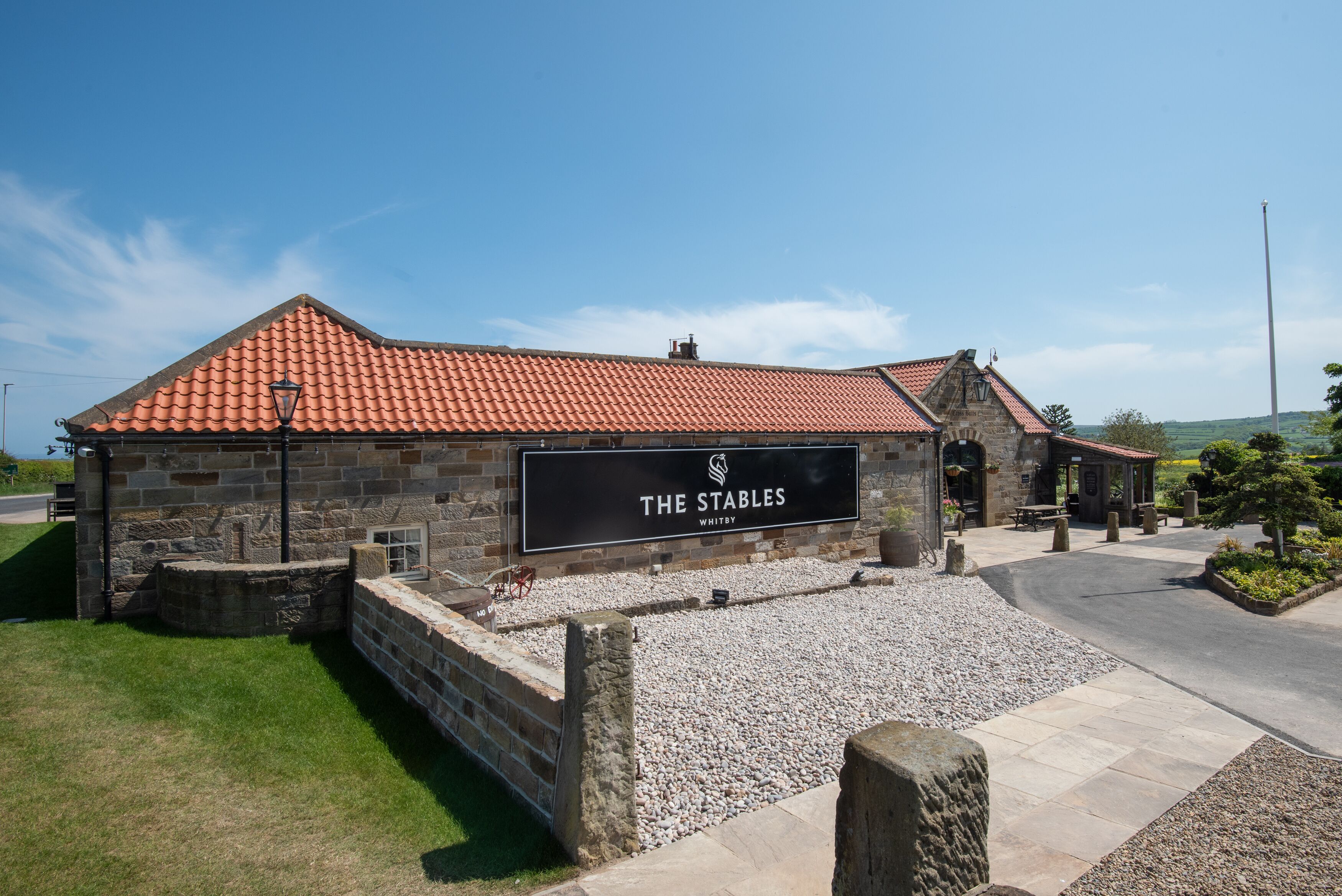 A stone building with a red-tiled roof and a sign that reads "The Stables."