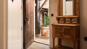 A wooden door leading to a stone-tiled patio with a large terracotta pot and a hanging plant. - The Stables Whitby (Whitby)