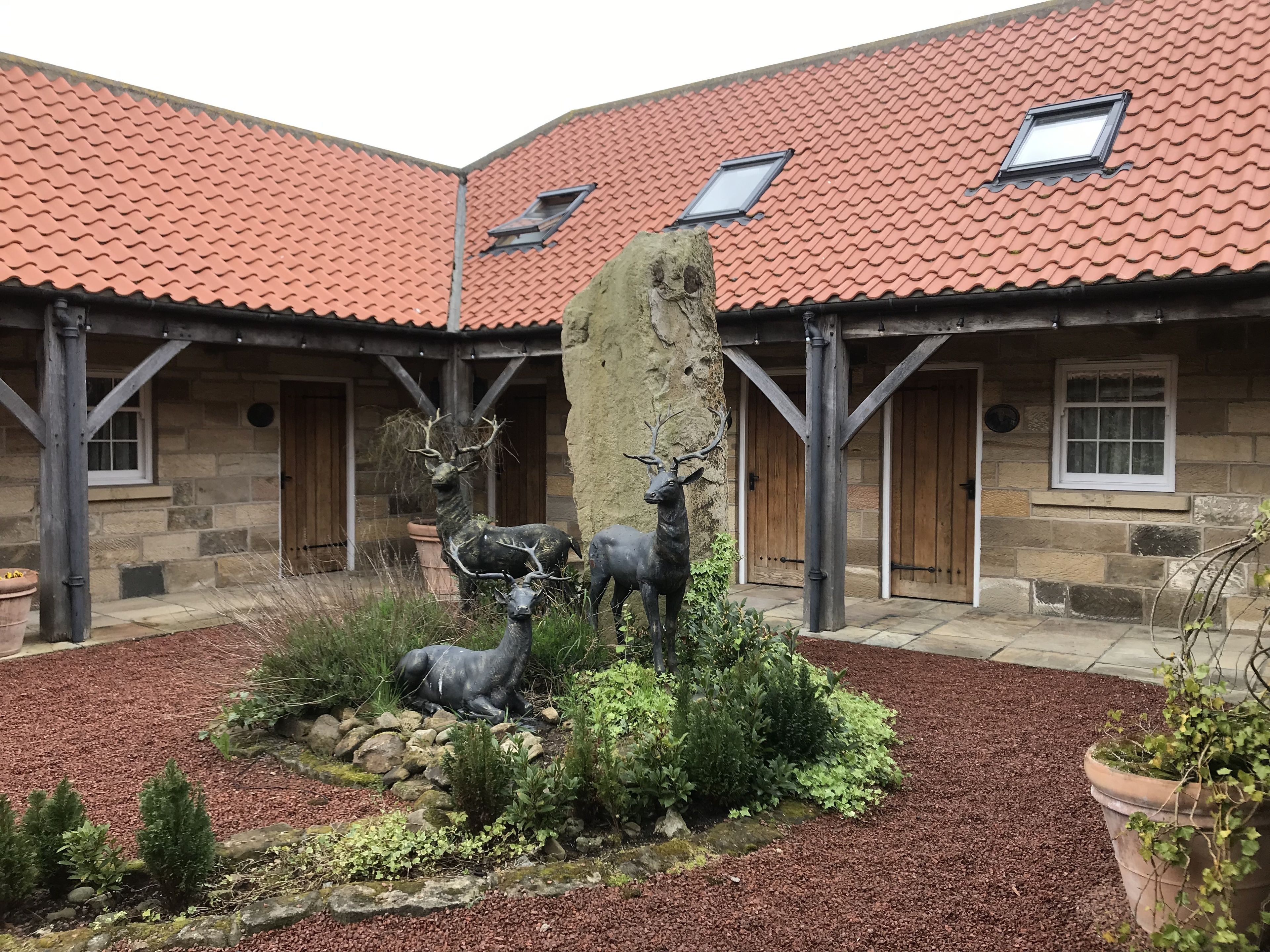 A courtyard with a stone building, a red-tiled roof, and a deer sculpture.