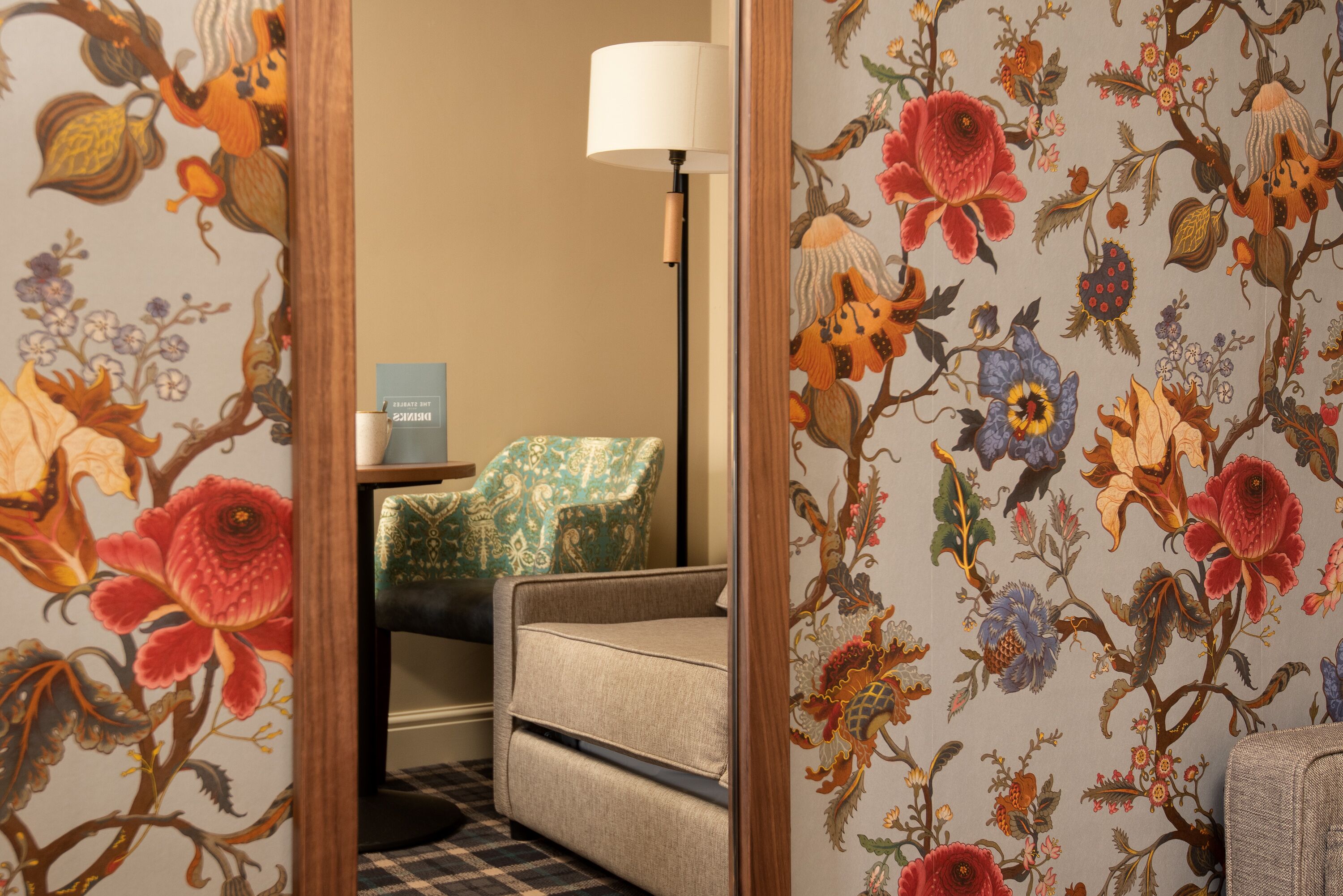 Une chambre d’hôtel avec un papier peint à motifs floraux, un canapé, un fauteuil et une lampe.