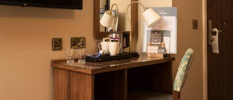 A hotel room with a wooden desk, a chair, a television, a mirror, and a menu board.