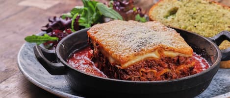 En portion lasagne i en gjutjärnspanna på en tallrik, serverad med en liten sallad och en bit bröd.