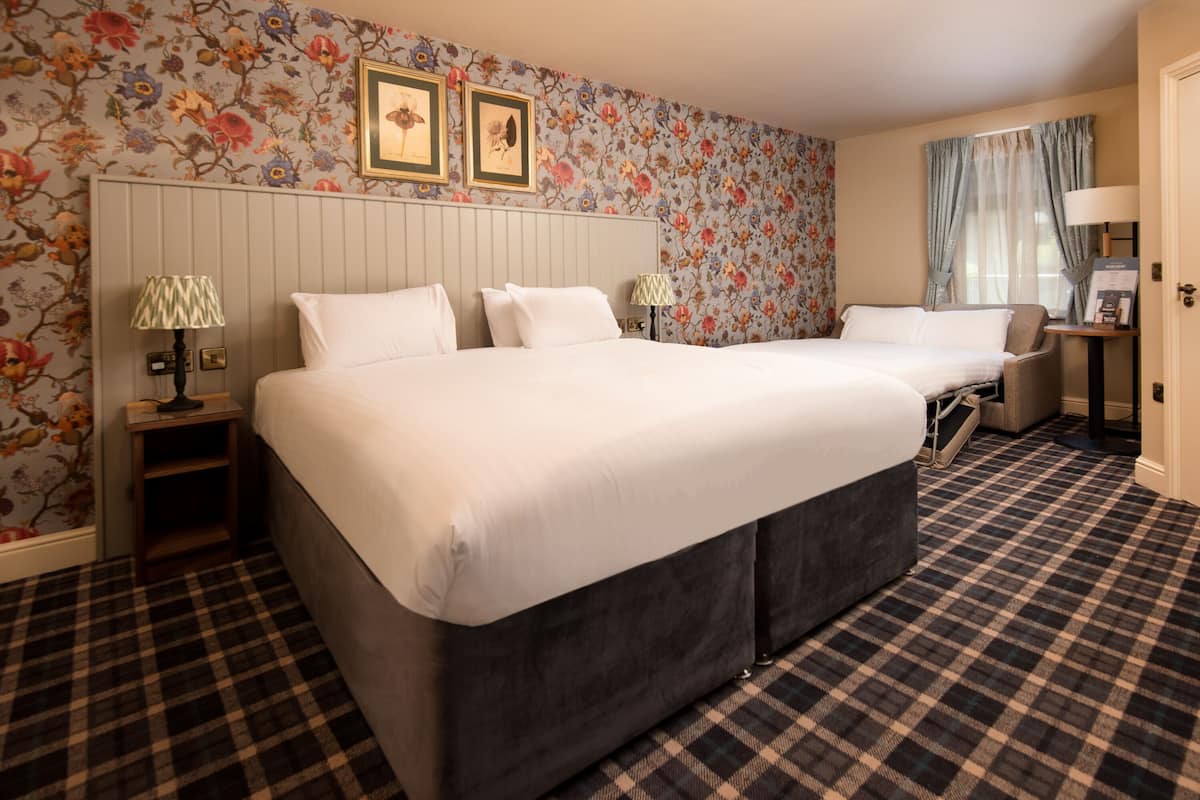 A hotel room with a large bed, two bedside tables with lamps, a chair, and a floral wallpaper design.