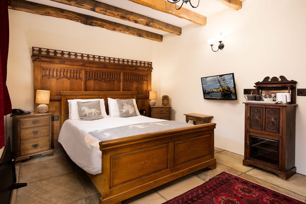 A wooden bed with a headboard, a nightstand, a small table, a cabinet, and a red rug.