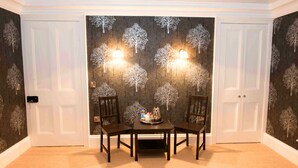 A dining area with a table set for two, flanked by two chairs, and a wall with a tree pattern wallpaper. - Bishopcleugh Guest House (Lockerbie)