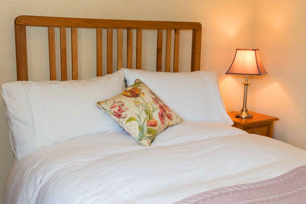 A bed with white linens, a floral pillow, and a bedside lamp.