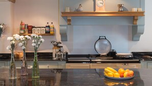 A modern kitchen with a black countertop, a wooden shelf with kitchen items, a clock, and a fruit bowl. - Bishopcleugh Guest House (Lockerbie)