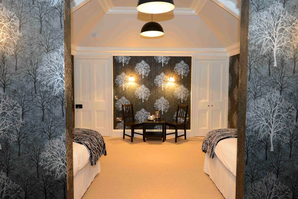 A hallway with a dining table and chairs, a chandelier, and a wall with a tree pattern.