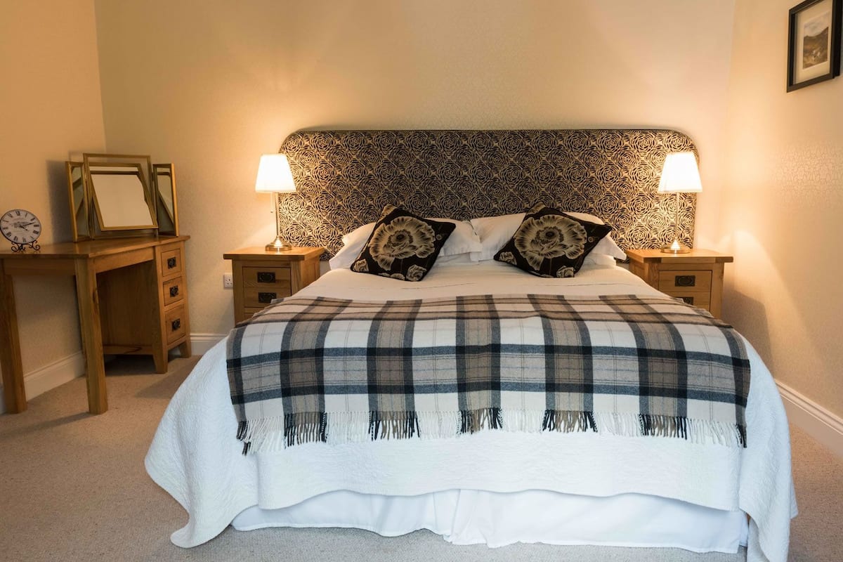 A bedroom with a large bed, two bedside tables with lamps, a wooden desk, and a clock.