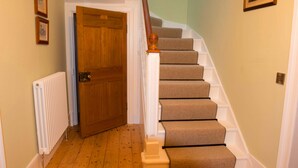 A wooden door with a brass doorknob, a white radiator, and a carpeted staircase with white handrails. - Bishopcleugh Guest House (Lockerbie)