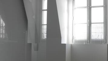 A room with wooden flooring, white walls, and a large window with blinds.