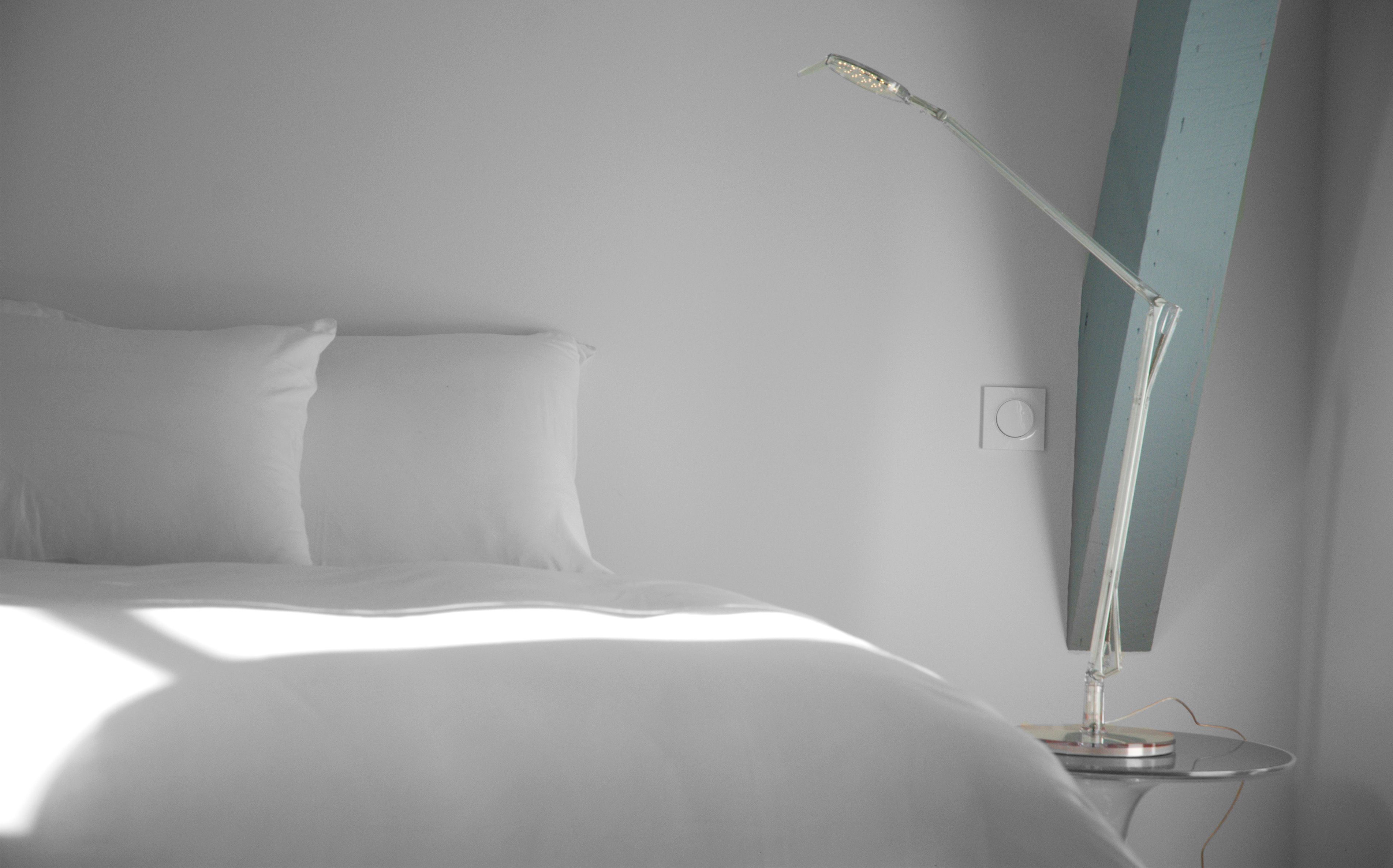 A minimalist bedroom with a bed, a bedside lamp, and a wall-mounted light fixture.