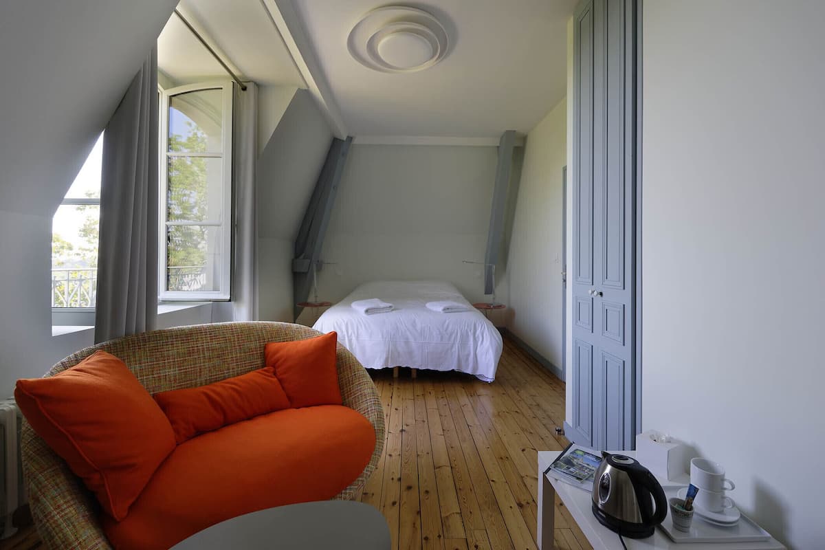 A room with a bed, a sofa, a table with a kettle and cup, and a window with curtains.