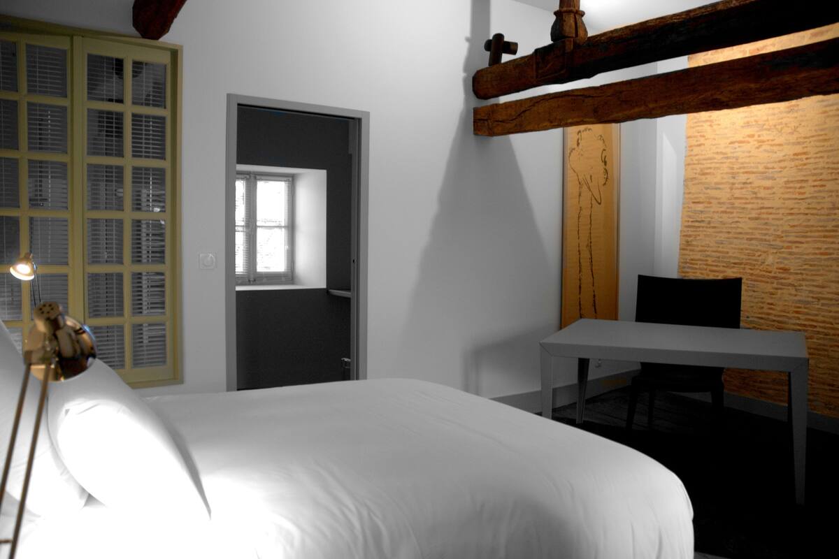 A bedroom with a bed, a desk, and a window.