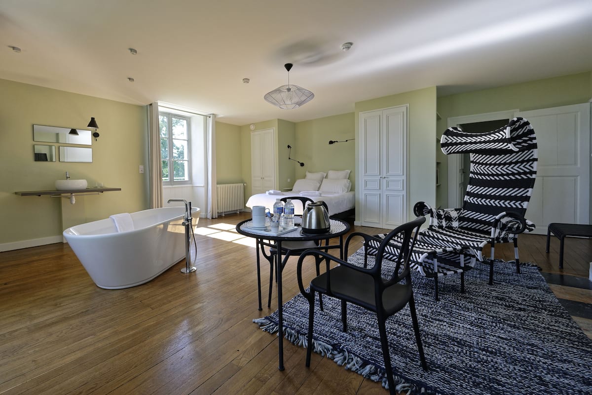A modern bathroom with a freestanding bathtub, a round table with a kettle, and a black and white patterned chair.