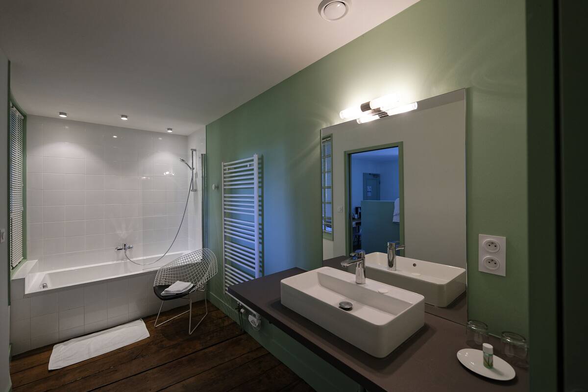 A modern bathroom with a bathtub, two sinks, a large mirror, and a shower.