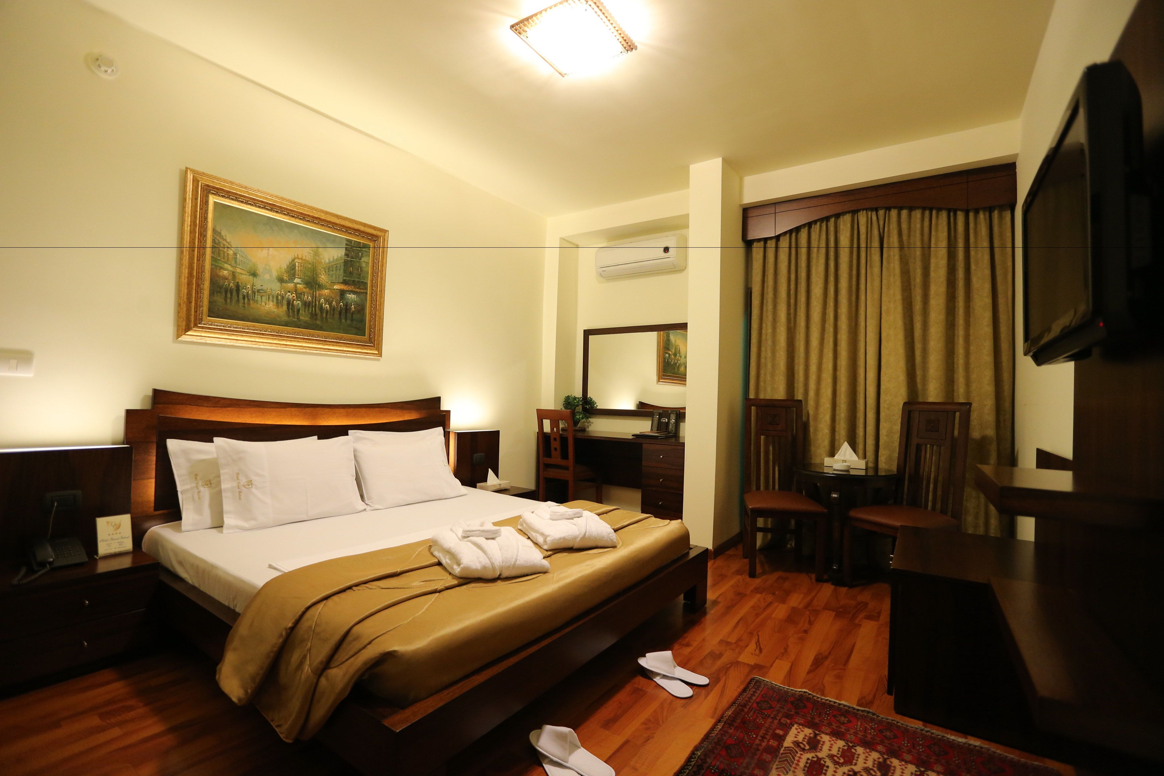 Habitación de hotel con una cama grande, un escritorio, una silla, un televisor y un cuadro en la pared.