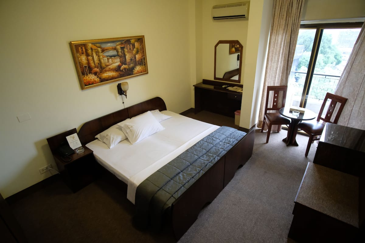Habitación de hotel con cama, escritorio, silla, un cuadro y ventana con cortinas.