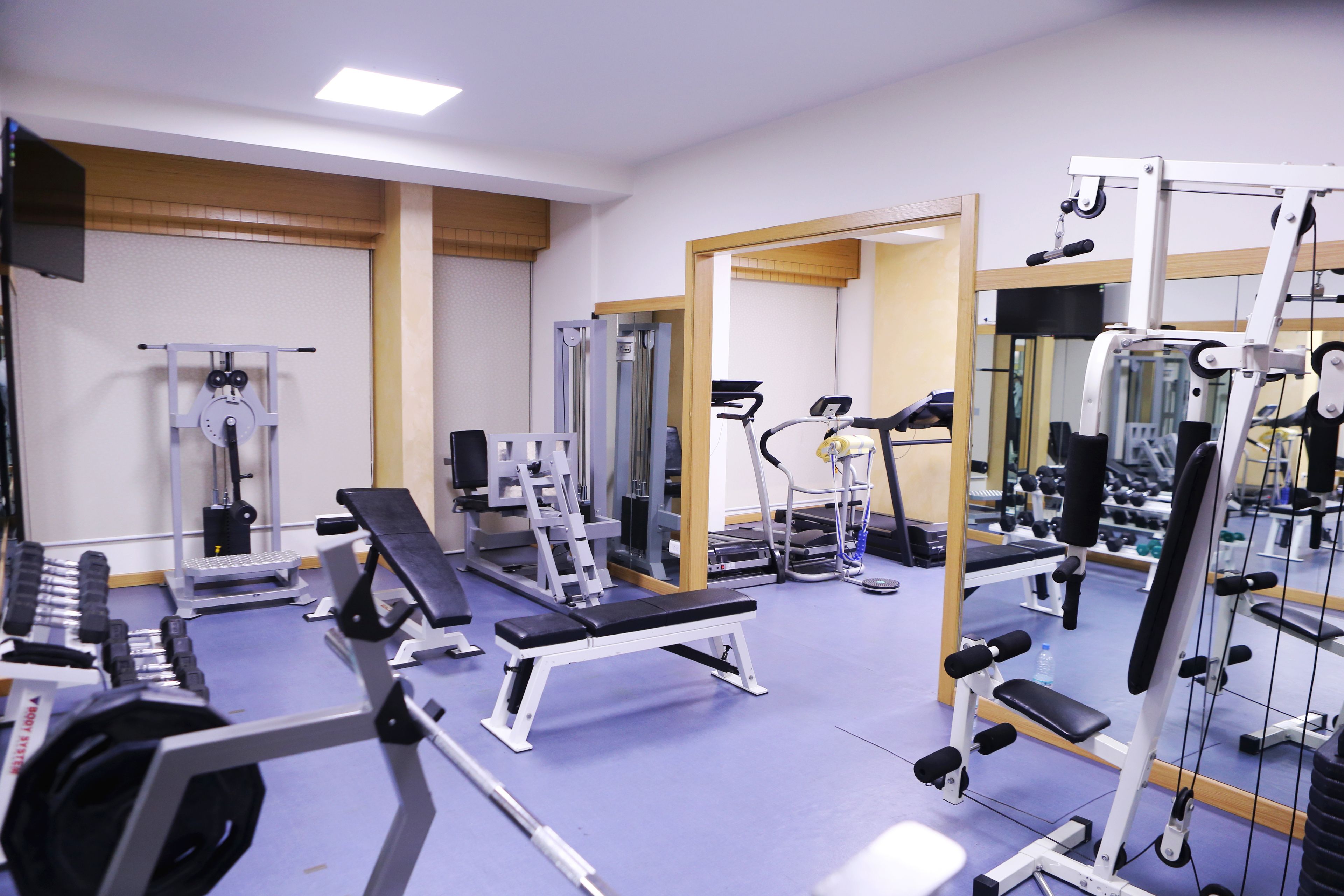 Een sportschool met diverse fitnessapparaten, waaronder loopbanden, krachttoestellen en bankjes.
