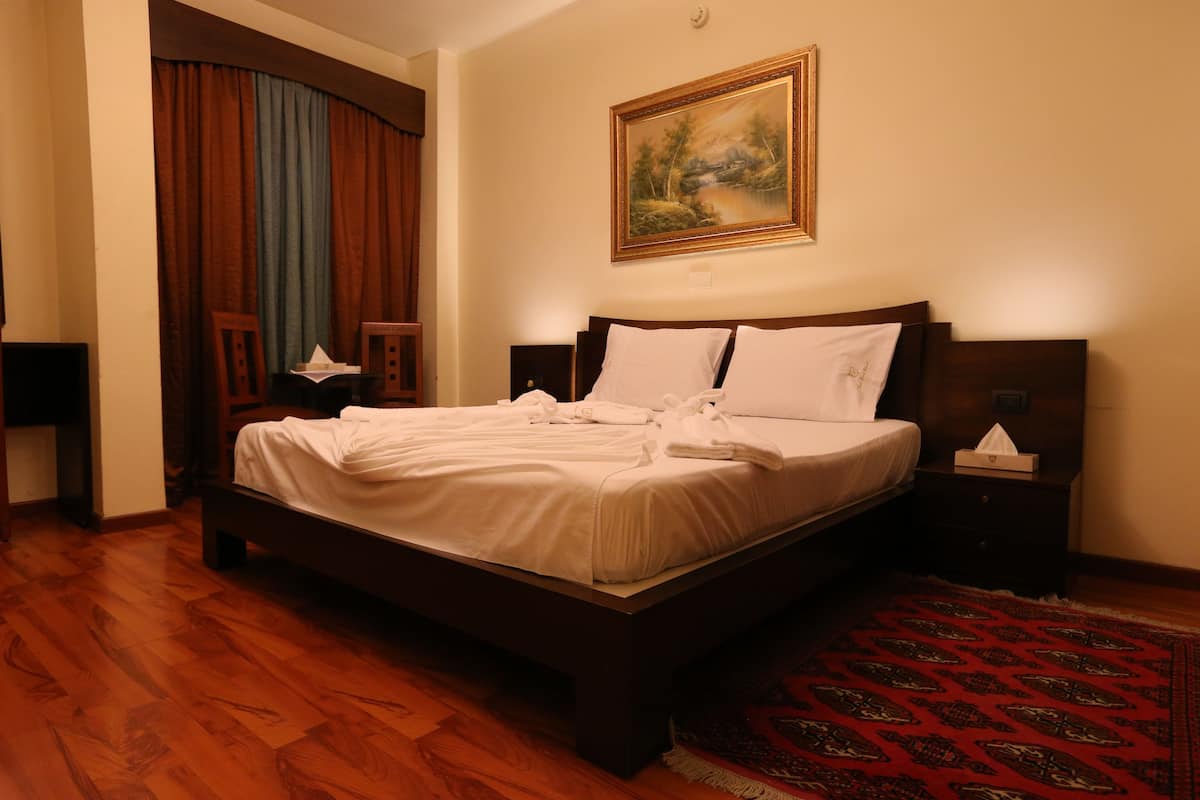 Una cama bien hecha con sábanas blancas, cabecera de madera y mesita de noche con caja de pañuelos.