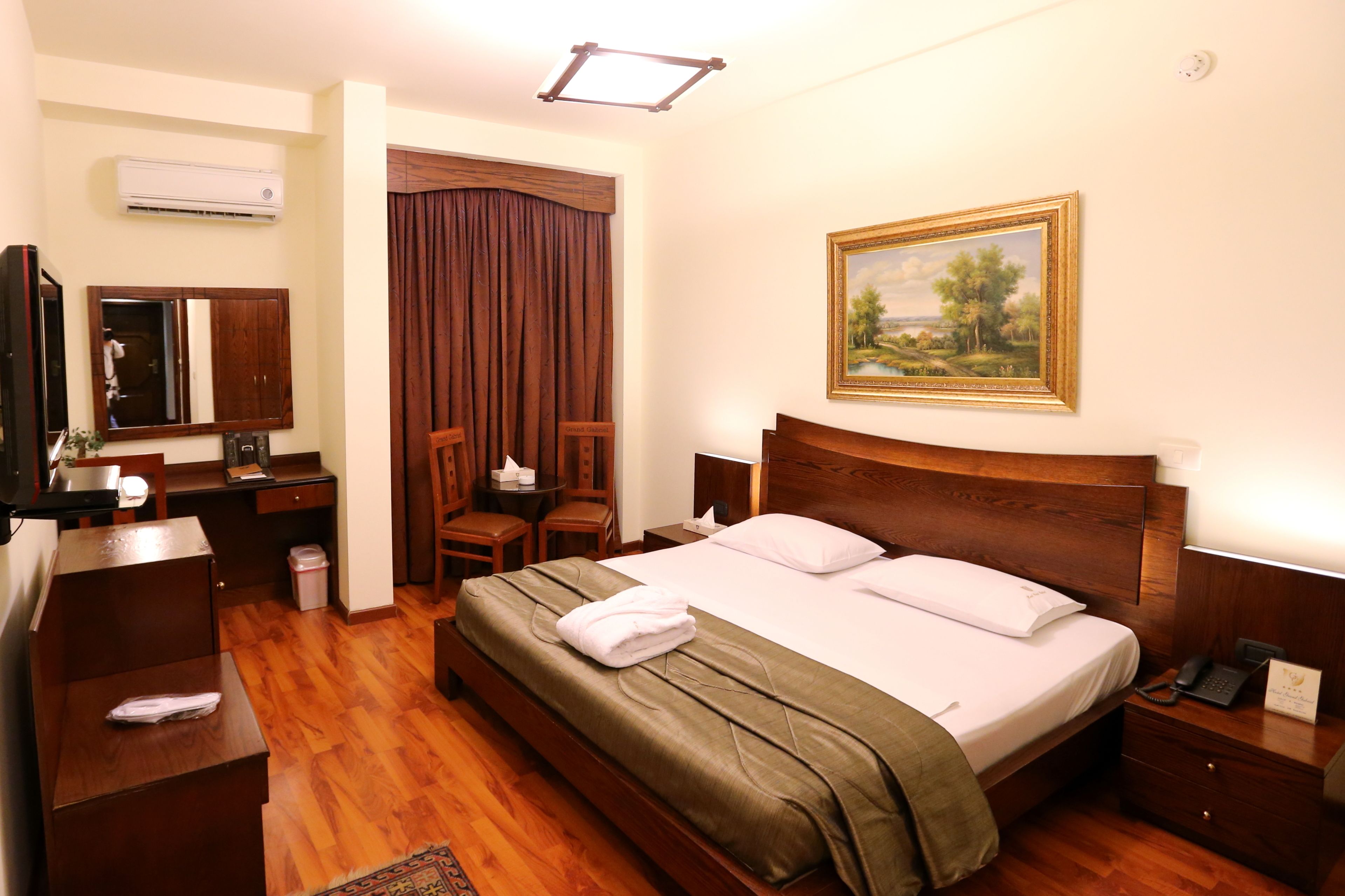 Una habitación de hotel con cama, escritorio, silla, televisión y aire acondicionado.