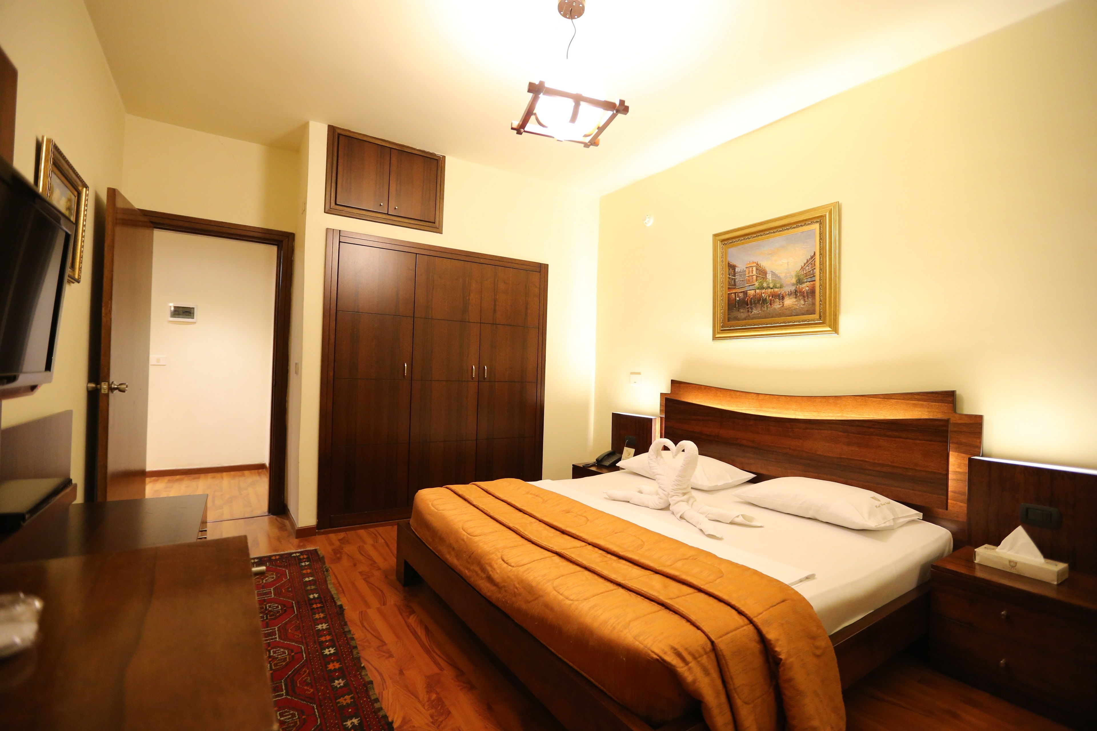 A hotel room with a wooden bed, a nightstand, a desk, a wardrobe, and a painting on the wall.
