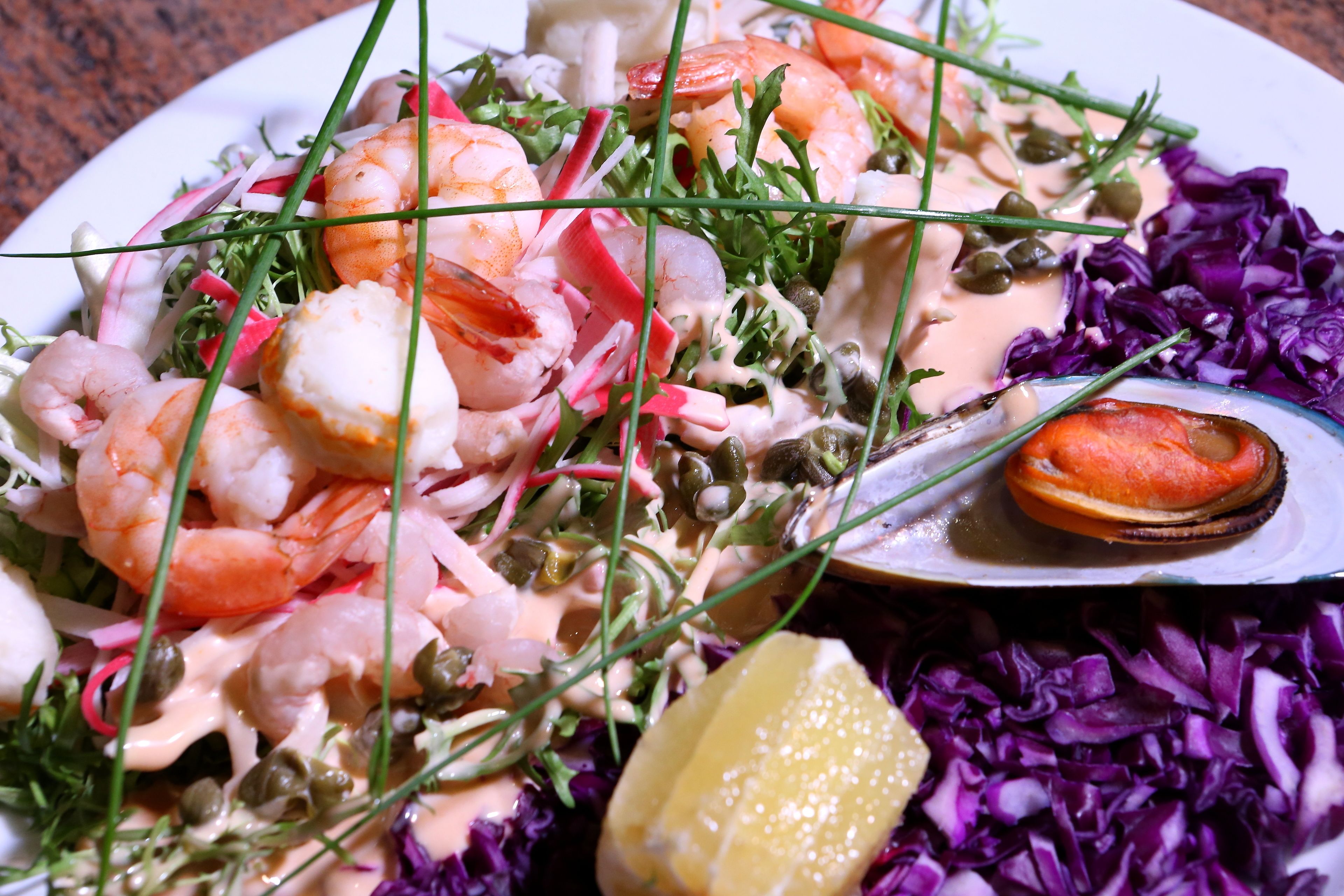 A plate of seafood salad with shrimp, radishes, and a lemon wedge.