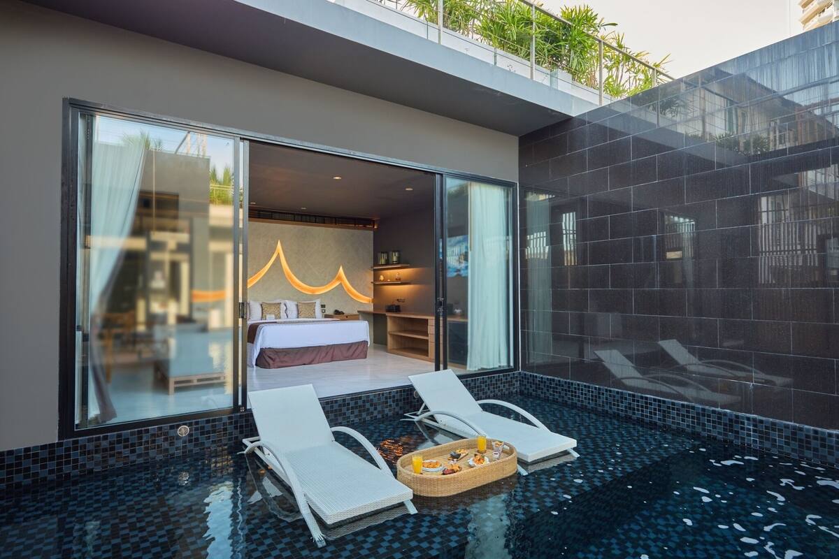 Ein modernes Hotelzimmer mit Glastür zu einem Balkon, einem kleinen Poolbereich mit Liegestühlen und einem Frühstücksbrettchen am Poolrand.