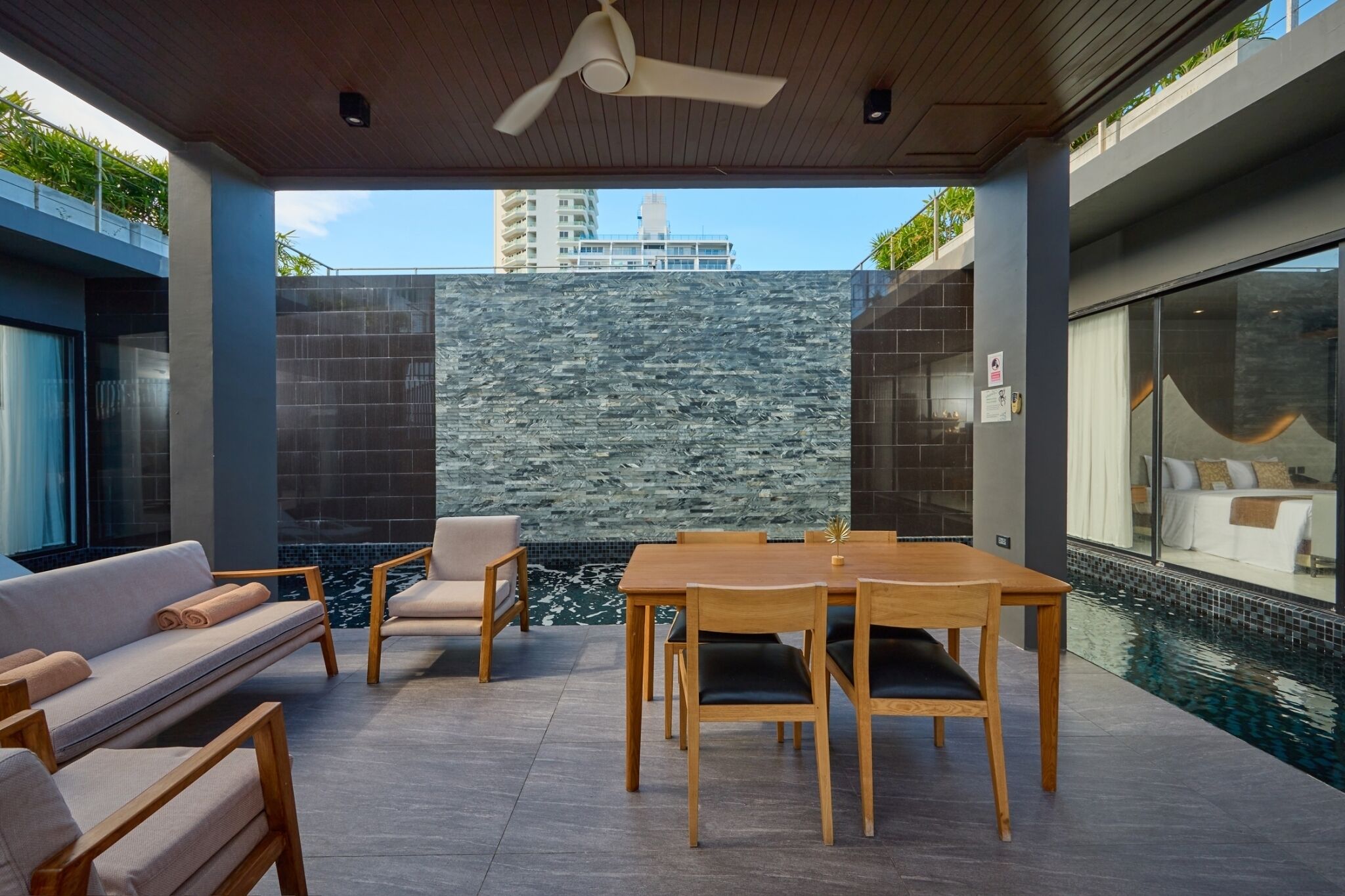 Un moderno espacio lounge al aire libre con piscina, mobiliario y un muro de piedra de fondo.