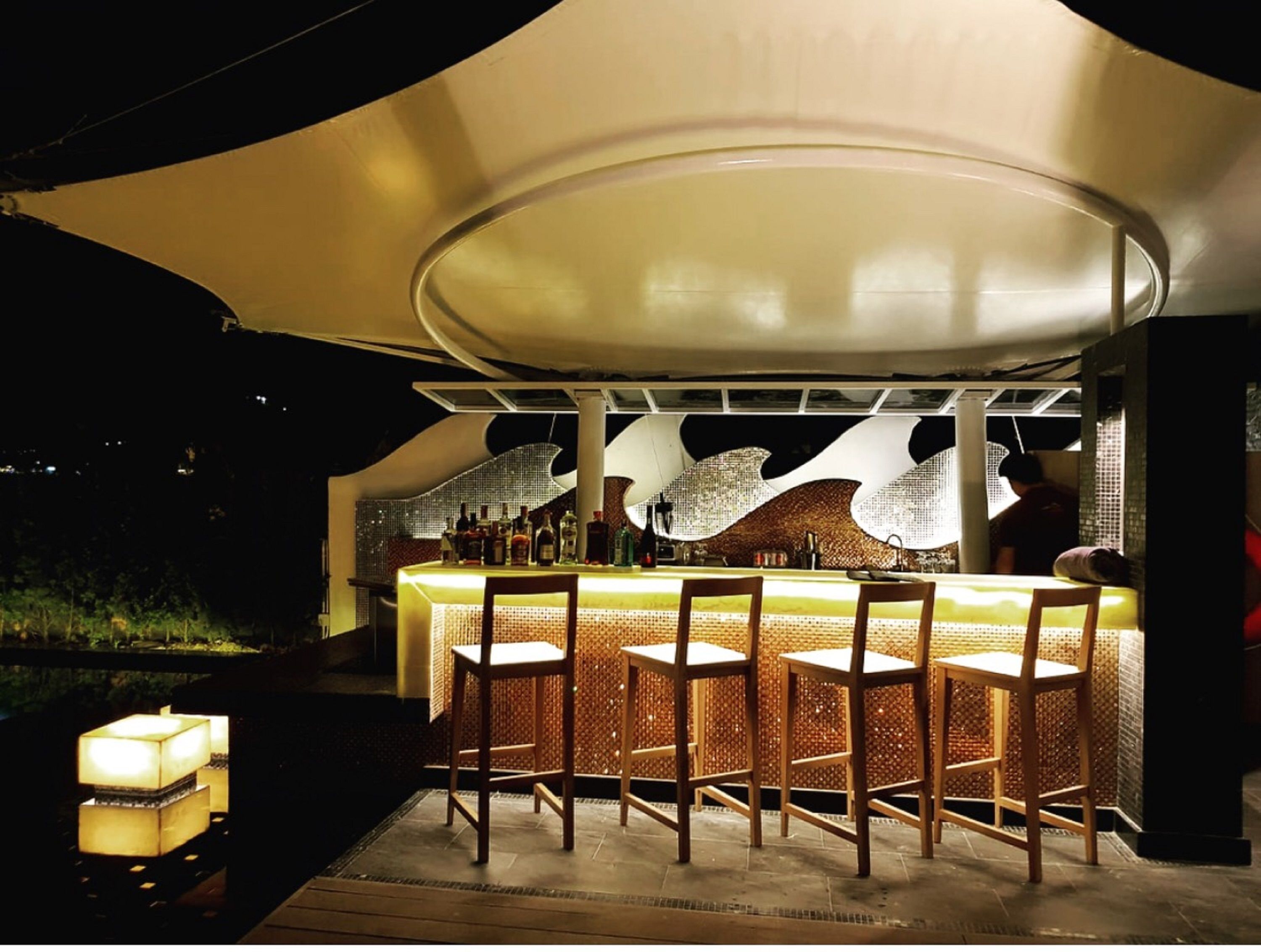 An outdoor bar area with a canopy, wooden chairs, and a bar counter with bottles.