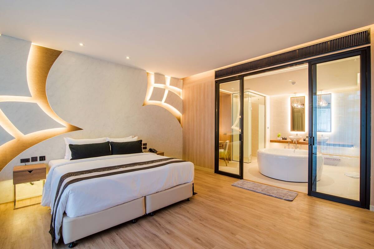 Ein modernes Hotelzimmer mit einem großen Bett, einem durch eine Glaswand abgetrennten Badezimmer und einem außergewöhnlichen Deckenstil.