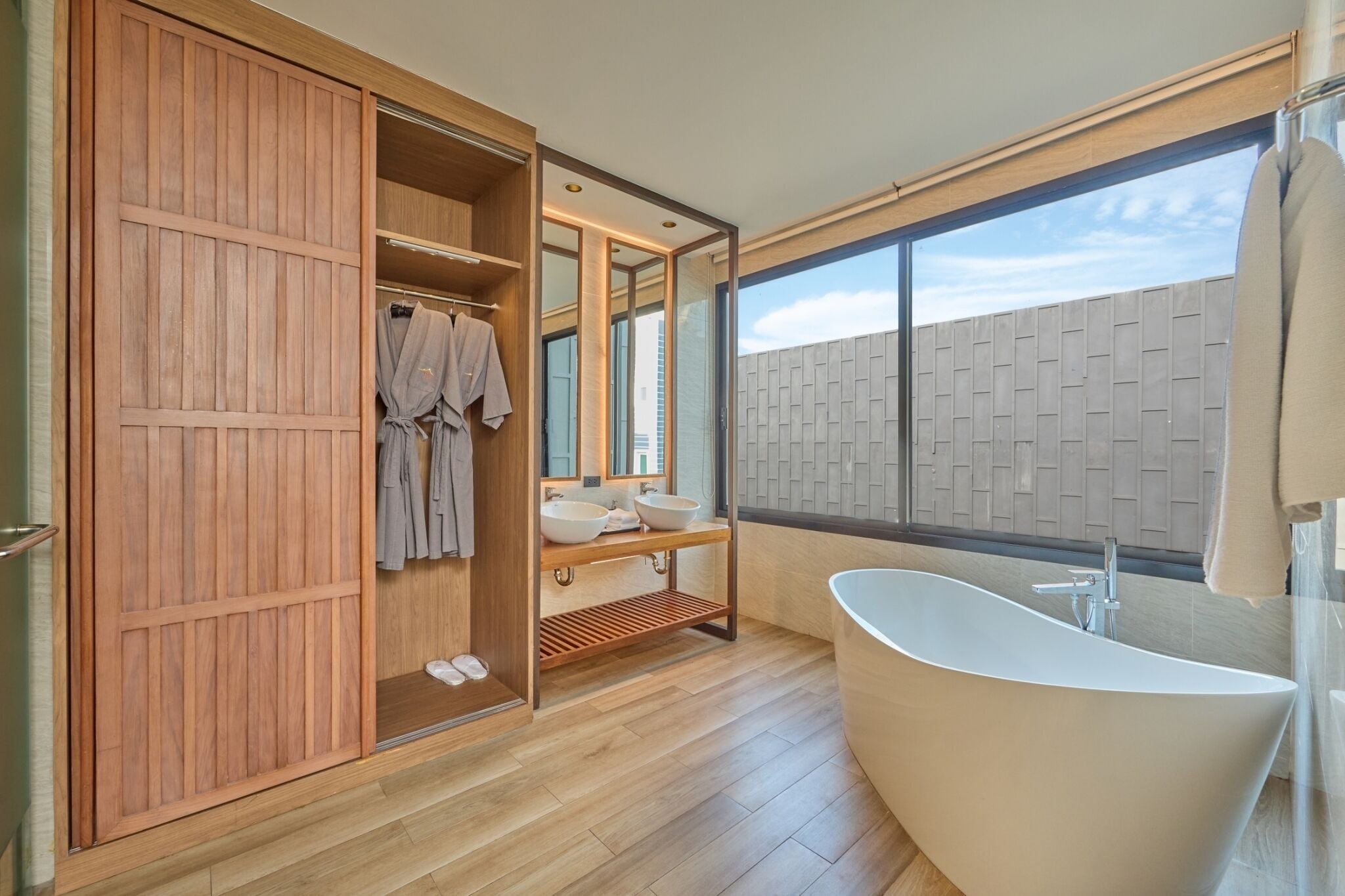 Een moderne badkamer met een vrijstaand bad, een houten garderobe en een grote spiegel.