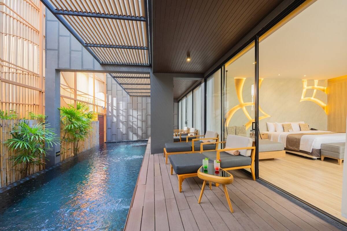 Ein modernes Hotelzimmer mit einer großen Glaswand, einem privaten Balkon mit Pool und einer gemütlichen Sitzecke.
