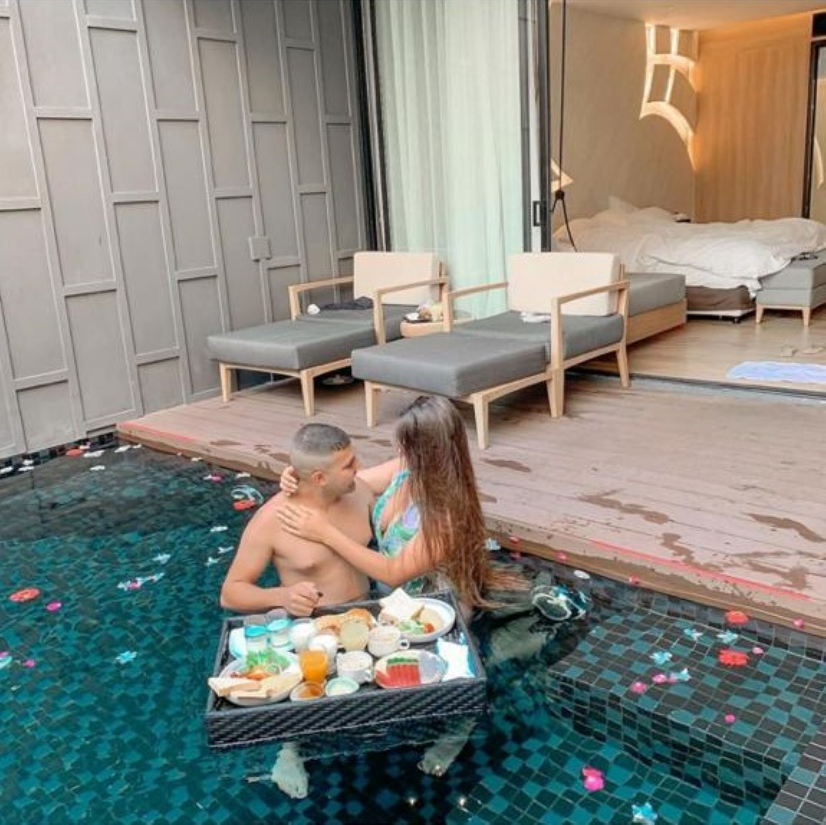 A poolside setting with a dining table, lounge chairs, and a bedroom with a bed and a nightstand.
