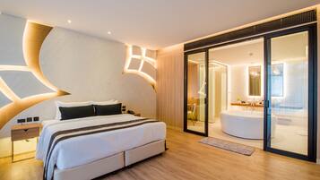 A modern hotel room with a large bed, a separate bathroom with a bathtub, and a sliding glass door leading to a shower area.
