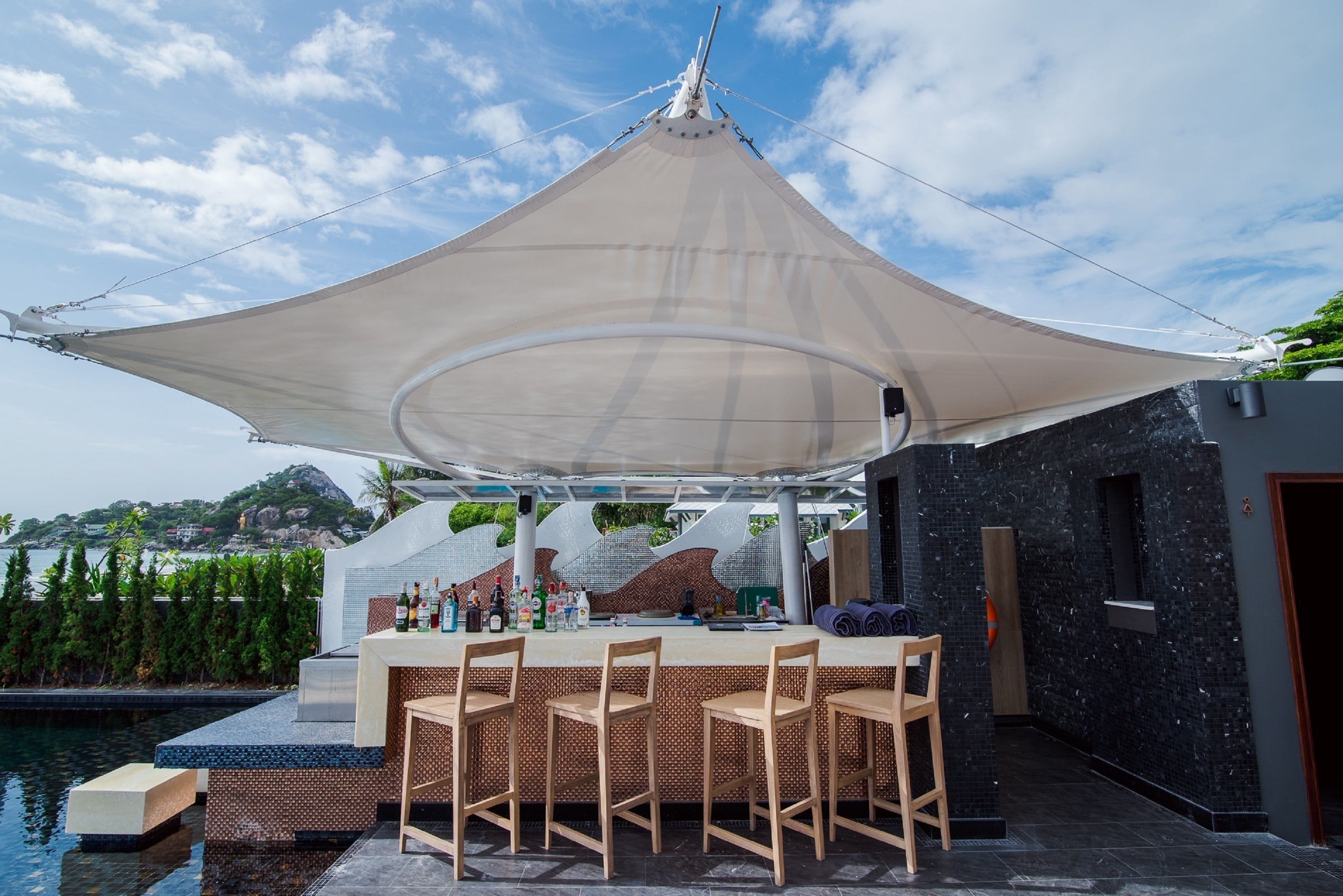 A bar area with a canopy, outdoor seating, and a pool.