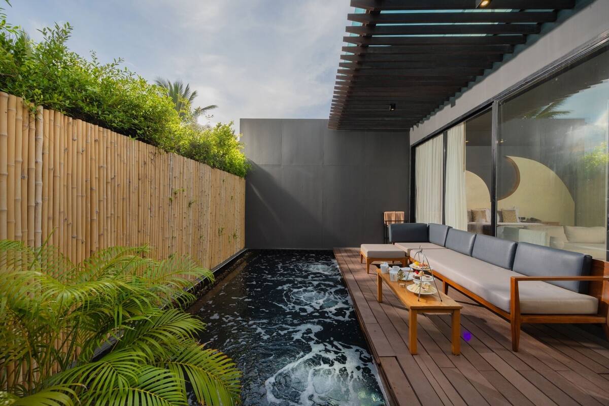 Ein moderner Außenbereich mit Holzterrasse, einer schwarzen Wasserspiels und einer Sitzecke mit Sofa und Tisch.