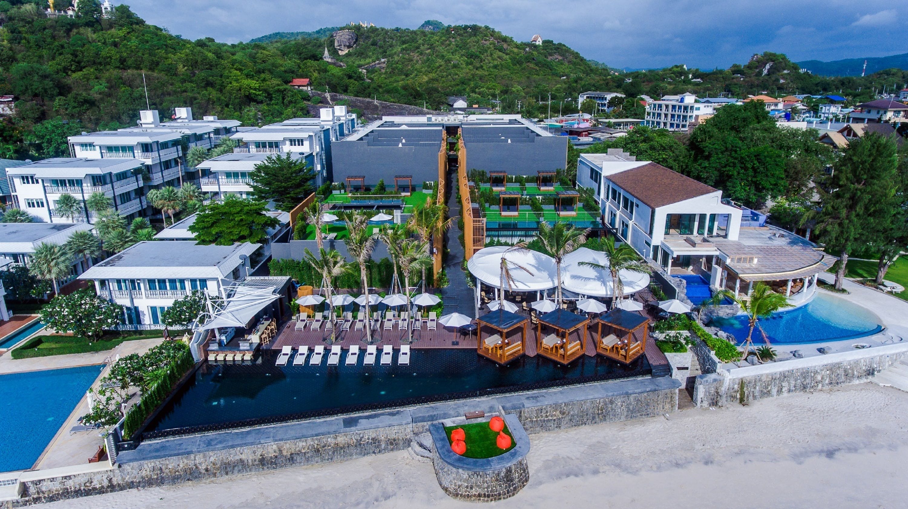 Un resort con piscina central, varias construcciones y montañas al fondo.